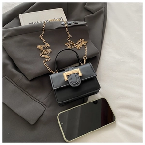 Close-up of black mini bag with gold U-buckle and chain strap on grey suit jacket