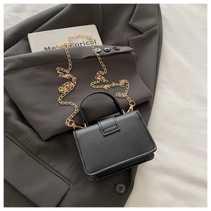 Detail of black crossbody bag with gold chain strap and textured leather on a grey blazer