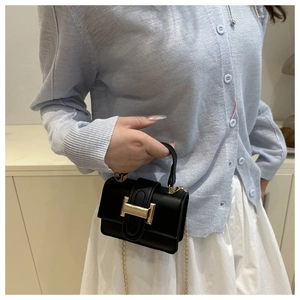 Detail of a black mini square crossbody bag with gold H-buckle on a blue sweater