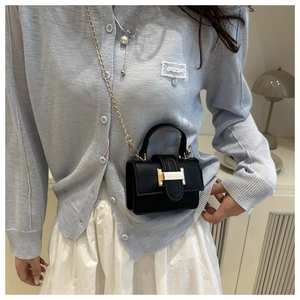 Dettaglio di una mini borsa nera chic con chiusura dorata e catena su un outfit elegante