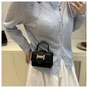 Close-up of black crossbody bag with gold metal H buckle and chain strap on model