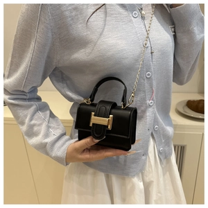 Detail of a mini black crossbody bag with a gold metal H buckle and chain strap