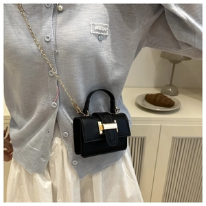 Detail view of black rectangular crossbody bag with gold chain strap on a model
