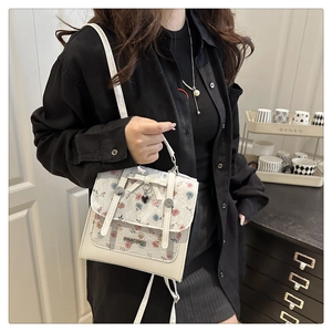 Detail of beige lace handbag with floral embroidery, elegant bow, and heart pendant charm