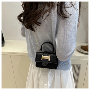Detail of a black mini square bag with golden H-shaped clasp and delicate chain strap