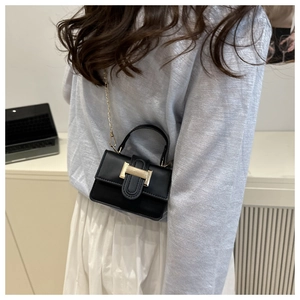 Detail of a black minimalist mini bag with gold hardware worn by a model
