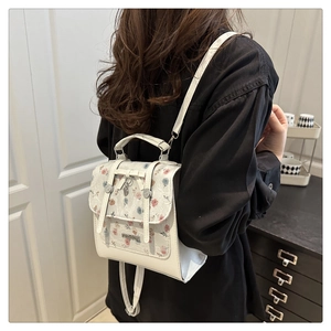 Detail of white leather mini backpack with floral lace flap and metal heart pendant