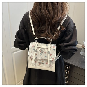 Detail of white lace backpack with floral patterns, bow accents, and heart pendant detail