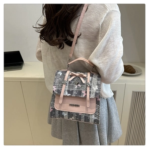 Detail of pink and grey plaid crossbody bag featuring a leather bow and metal heart charm