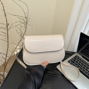Minimalist beige leather crossbody saddle bag shown on a desk with a laptop