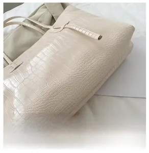 Detailed view of the wide bottom and crocodile texture on this cream tote bag