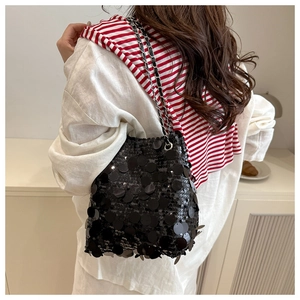 Detail of a black sequin bucket bag with a metal chain strap worn by a model