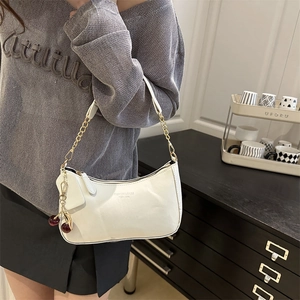 White faux leather hobo bag with gold chain and cherry charm shown on a model