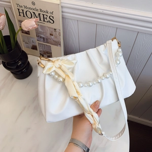 White ruched cloud shoulder bag with pearl chain and silk bow on marble table