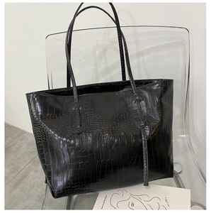 Detail of black crocodile pattern tote bag with long straps on a modern chair