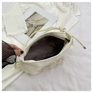 Dettaglio di ricamo a farfalla e nappa su borsa beige in un ambiente dallo stile di vita