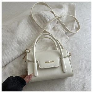 Detail of white PU leather square bag with gold FASHION text and top handles