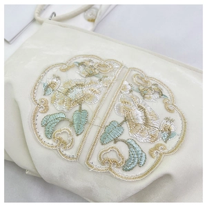 Dettaglio del ricamo floreale sul tessuto di raso color crema della borsa stile cinese
