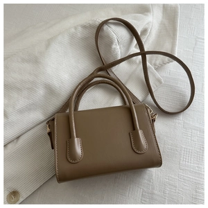 Detail view of brown square mini bag with dual top handles on corduroy background