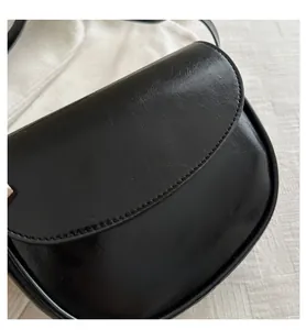 Close-up of black glossy leather saddle bag with detailed stitching and flap design
