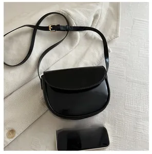 Black saddle bag size comparison with smartphone on cream corduroy background