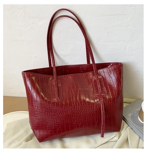 Close-up of deep red tote bag with crocodile texture and glossy faux leather finish