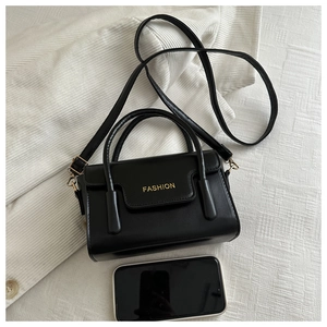 Top view of black matte leather handbag with gold 'FASHION' text and smartphone for scale