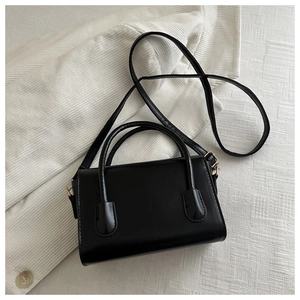 Detail of minimalist black handbag with golden hardware on a corduroy fabric background