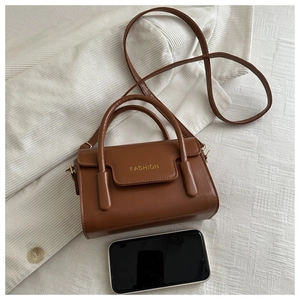 Brown leather crossbody bag detail with gold FASHION text and smartphone for size scale