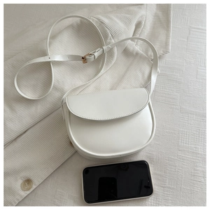 Detailed view of cream-white saddle bag with gold metal buckle and adjustable shoulder strap
