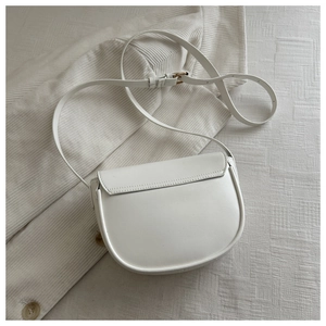 Overhead view of a minimalist white saddle bag with adjustable strap on cream textured fabric