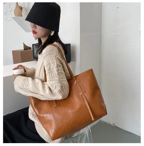 Detail of orange brown tote bag featuring luxury crocodile texture and long shoulder straps
