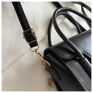 Detail of black PU leather handbag with gold metal buckles and slim round handles