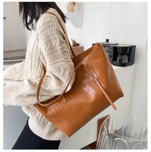 Brown crocodile pattern tote bag shown from side on shoulder with knit sweater