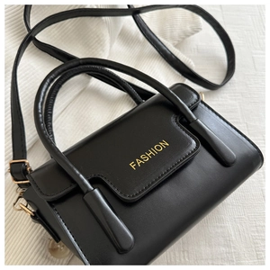 Detail view of black leather handbag with gold fashion lettering and metal hardware