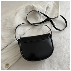 Close-up of black semi-circular saddle bag with glossy texture and golden metal hardware