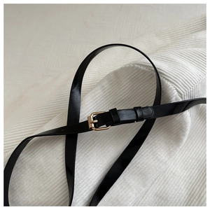 Close-up of a slim black faux leather belt with a golden square buckle on white fabric