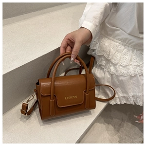Brown faux leather crossbody bag with golden Fashion logo on outdoor stairs detail