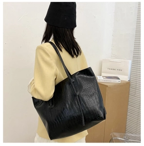 Detail of black crocodile pattern tote bag shown from a side-view on a model