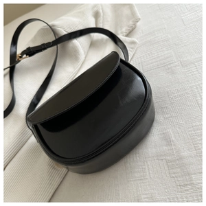 Detail of minimalist black patent leather saddle bag on white textured fabric background