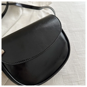 Close-up of a black saddle bag featuring smooth faux leather and silver metal buckles
