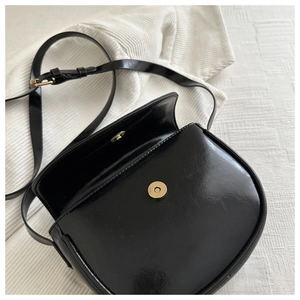 Detail of black leather saddle bag showing the magnetic buckle and glossy material texture