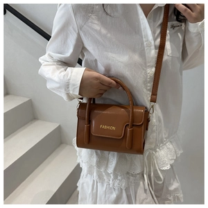 Detail of caramel brown square handbag with gold fashion text and top handles