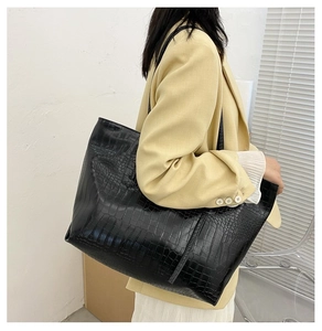 Side view of black crocodile pattern tote bag carried by model in a minimalist setting