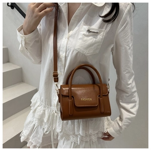 Detail of caramel brown crossbody bag featuring golden Fashion logo and metal hardware