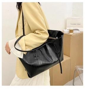 Detail of black crocodile texture tote bag styled with yellow blazer and white skirt