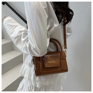 Caramel leather crossbody bag with FASHION gold lettering on white dress backdrop