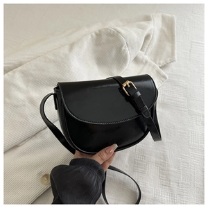 Detail of the black semi-circle saddle bag with shiny finish and golden pin buckle clasp