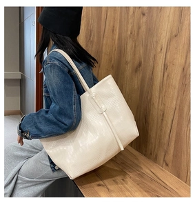 Detail of cream crocodile pattern tote bag shown from a side angle on a shoulder