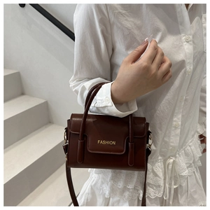 Detail of dark brown leather mini bag with Fashion text and top handle on a model